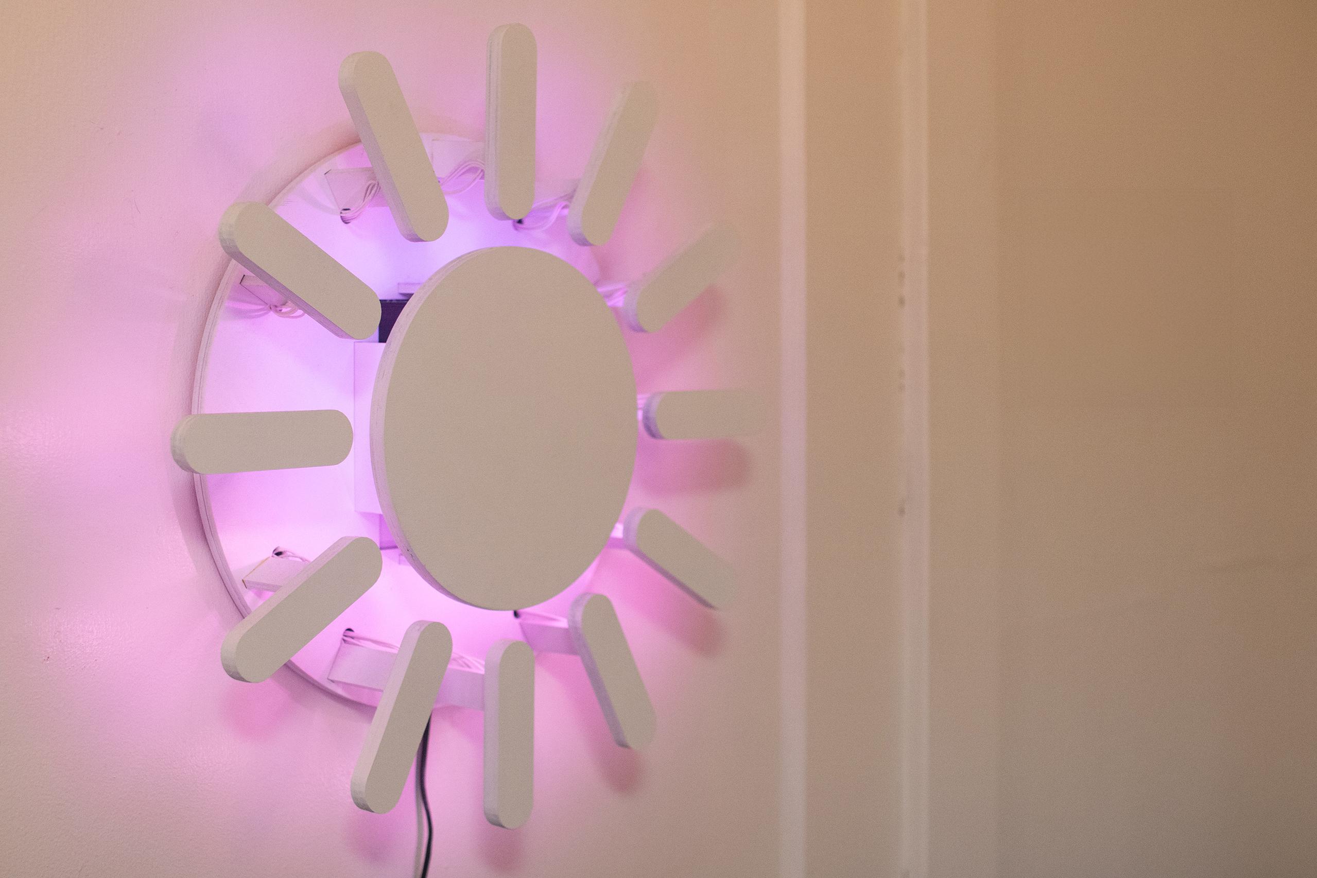 The Sun Clock is shown glowing with sunrise colors on a white wall.