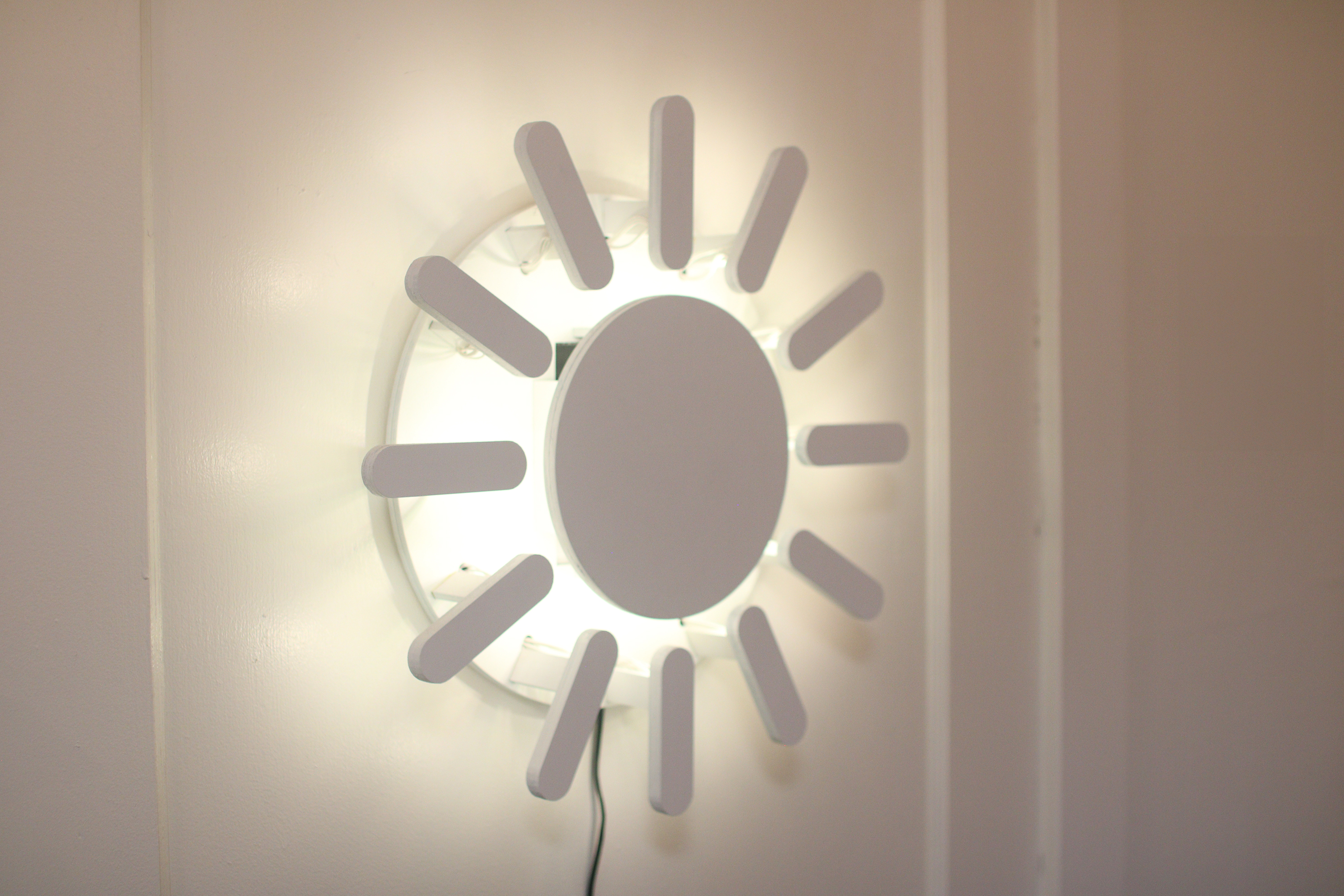 The Sun Clock is seen hanging on a wall, glowing from behind with a warm, white light.