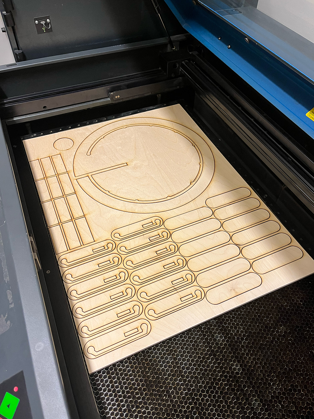 A sheet of plywood is laying in a laser-cutter bed after being cut.